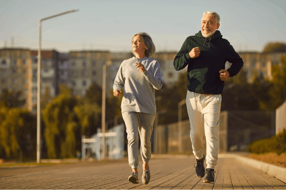 Two older adults jogging together on a paved path with a cityscape in the background